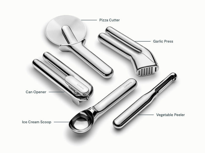 The Caraway 5-Piece Stainless Steel Kitchen Gadget Set includes a pizza cutter, garlic press, can opener, ice cream scoop, and vegetable peeler—each labeled for easy use on a white background.