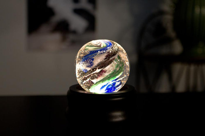 Illuminated swirled glass orb on a black stand with a warm glow from below