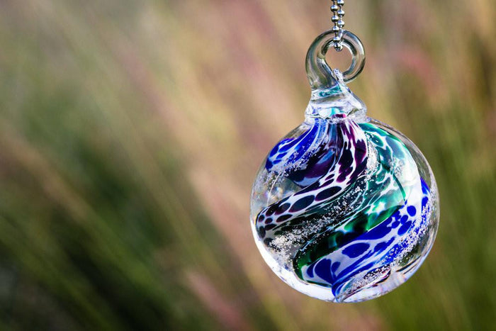 Blue green purple swirled cat eye cremation orb suspended from a metal loop on a silver chain