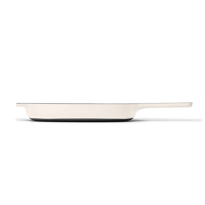 The 10.5 Cast Iron Grill Pan by Caraway features a sleek, modern design with a long handle. It offers superior heat retention and has a light exterior that contrasts with the dark base, elegantly highlighted against a plain white background.