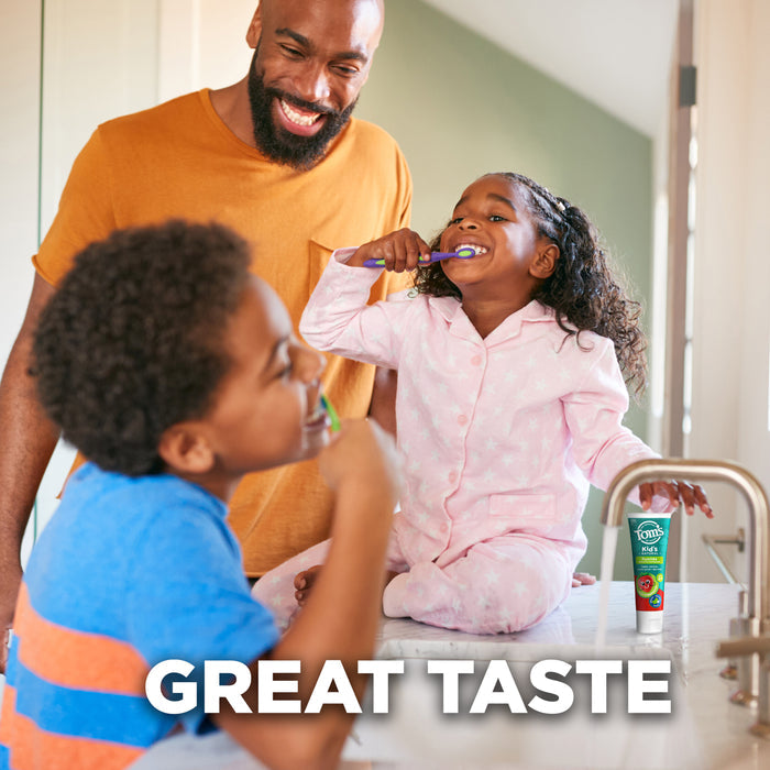 A man smiles at a young girl sitting on a bathroom counter in pink pajamas, brushing her teeth. A boy in a blue shirt brushes his teeth nearby. A tube of toothpaste is next to the girl. Bold text reads, "GREAT TASTE.