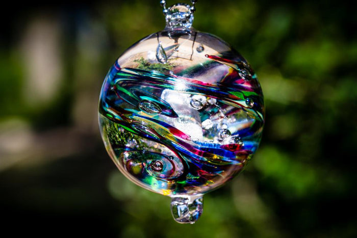 Side view of a dark confetti glass orb with embedded cremation ashes and vivid multicolored swirls.