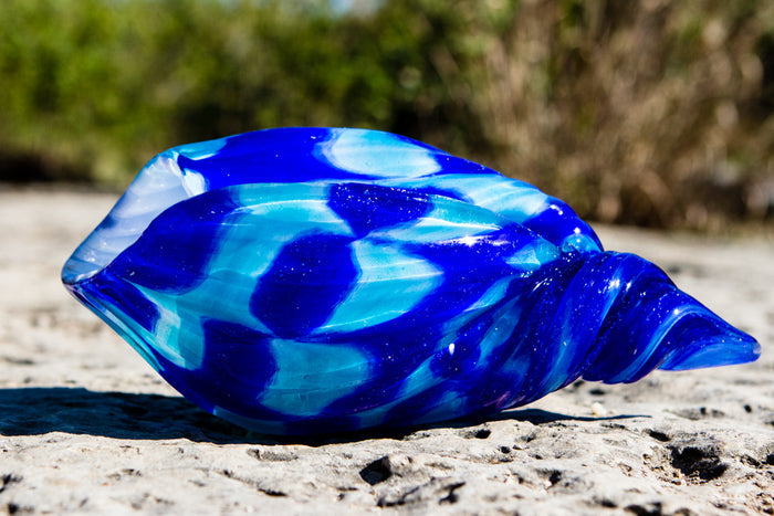 Blue glass seashell on sandy ground with a blurred natural background