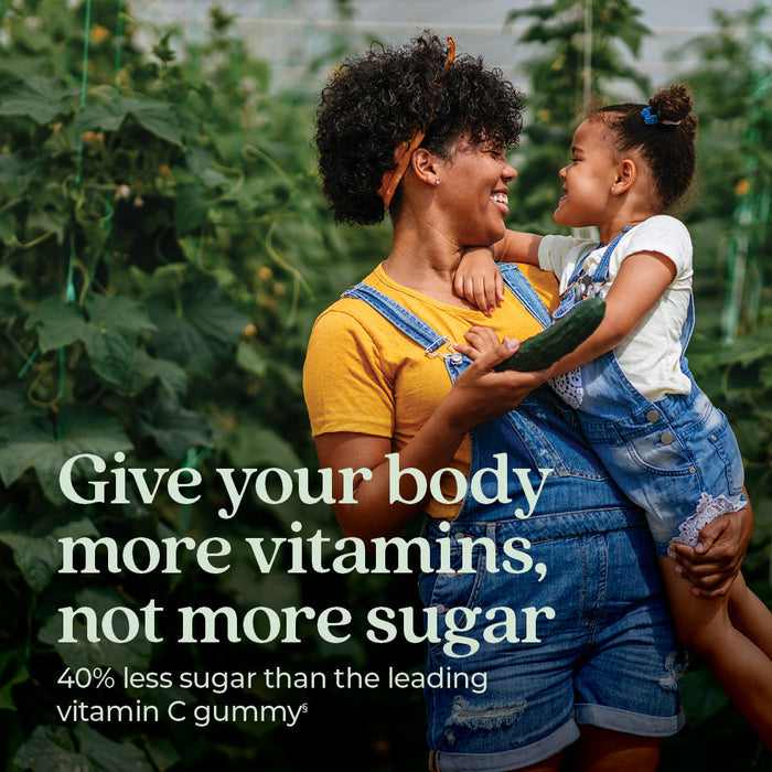 A smiling woman in overalls holds a young girl near green plants. The girl touches her face. Text: Support immune defense with New Chapter Immune Defense Vitamin C+ Gummies, Citrus Flavored—40% less sugar, organic Blue Agave fiber.