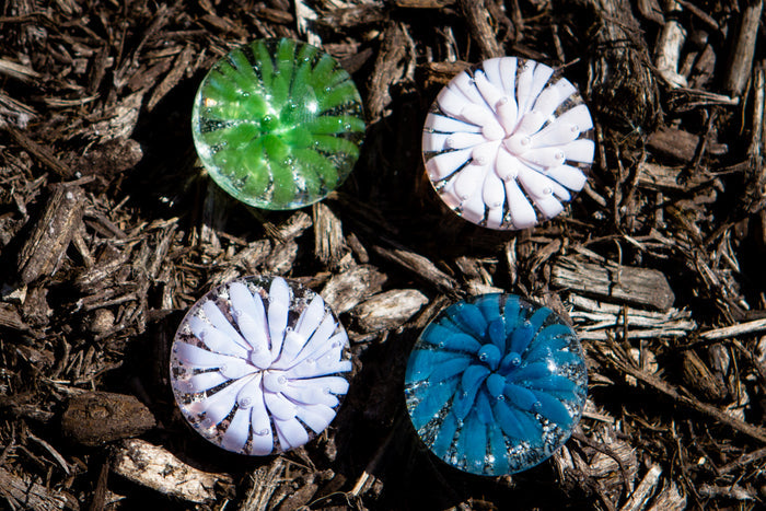 Keepsake flower stones infused with cremains in green white and blue tones arranged on wood mulch.
