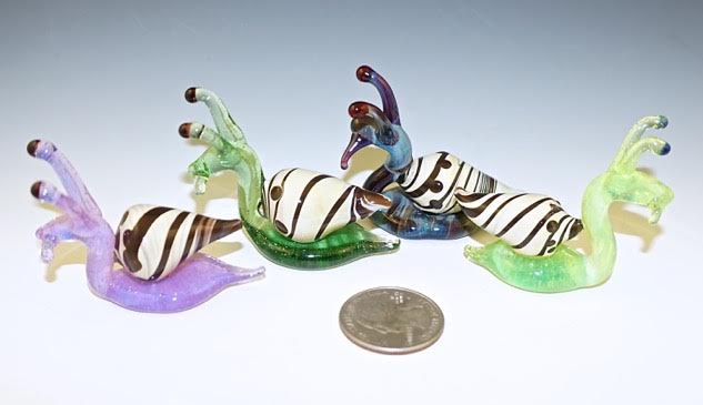 Glass memorial snail approx 1.5 inches tall by 2 inches long with cremains infused in the underside and colored bodies in purple green or blue.