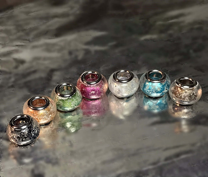 Colorful metallic cremation beads with inner metal cores arranged in a row for Pandora bracelets.