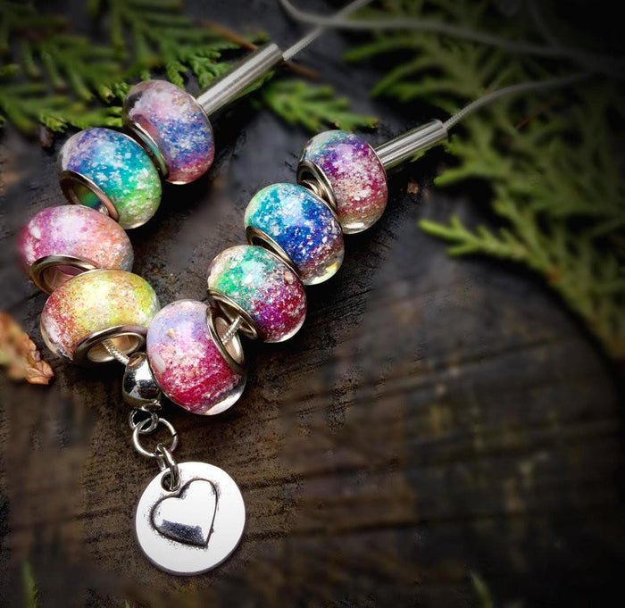 Rainbow's Bridge necklace shown on a wood surface with eight colorful infused beads and a round heart pendant