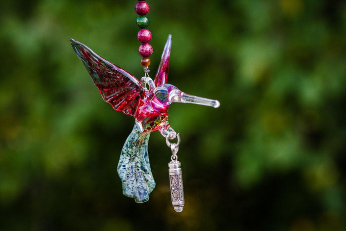 Glass hummingbird pendant with pink wings on a pink agate and jade bead necklace, with a dangling ornate silver keepsake urn.