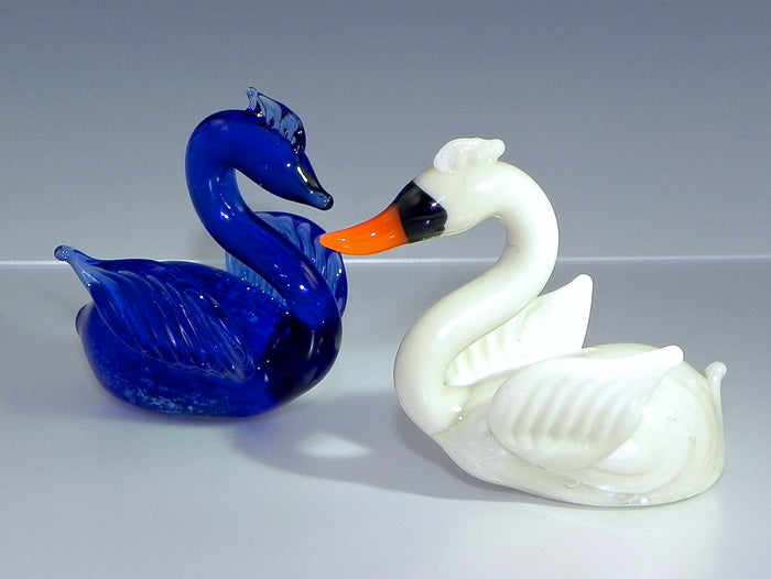 Two glass swans facing each other, one cobalt blue and one white with an orange beak.