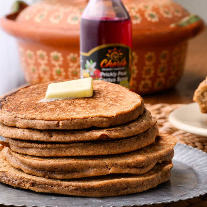 Stack of pancakes with butter and a bottle of syrup on a wooden table.