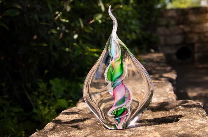 Clear glass memorial flame with a spiral tri color design containing cremation ashes.