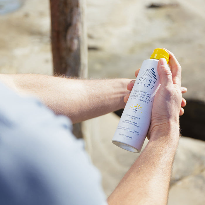 Someone holds Oars + Alps 100% Mineral Antioxidant Sunscreen Spray - SPF 30 outdoors, ready to apply its antioxidant-rich formula in the sun.