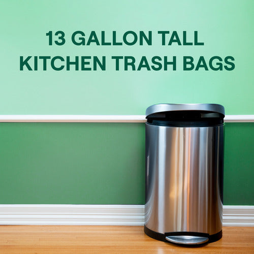 Against a green wall with white trim, on a wooden floor, stands a stainless steel kitchen trash can. Text above reads: Seventh Generation 13 Gal Tall Kitchen Drawstring Trash Bags with Genecore® 3-layer technology for tear resistance.