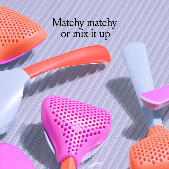 Colorful hairbrushes with pink and orange perforated heads and pastel handles are arranged on a striped surface. The text "Matchy matchy or mix it up" is displayed above the brushes.