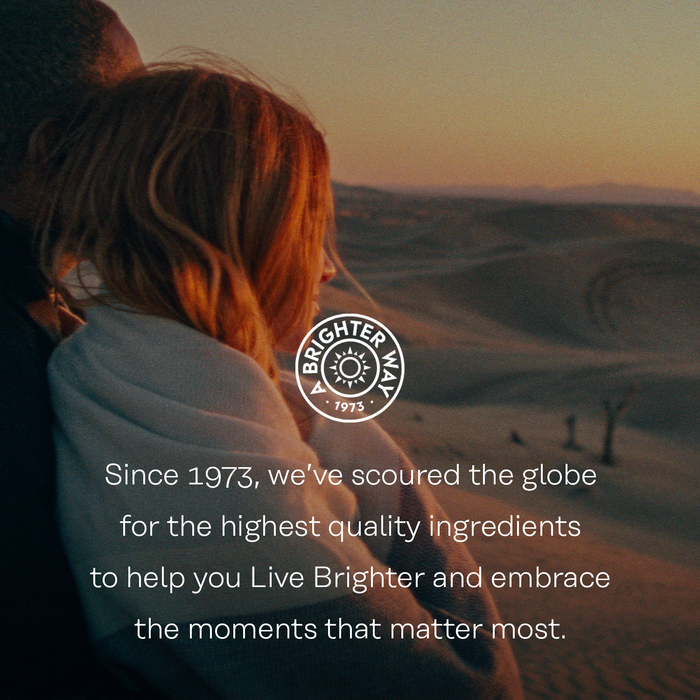 A person with long hair is wrapped in a blanket, embracing another person while overlooking a desert landscape during sunset. The text reads: "Since 1973, we’ve scoured the globe for the highest quality ingredients to help you Live Brighter and embrace the moments that matter most.