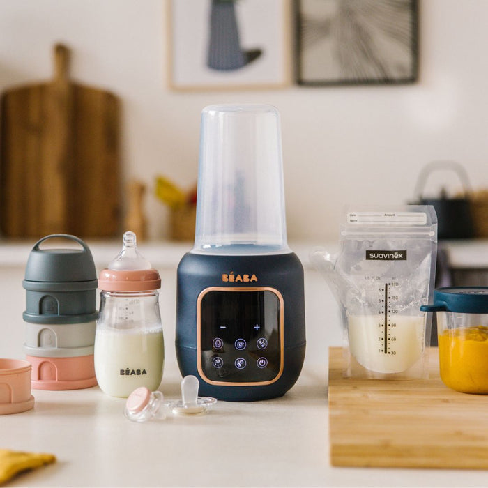 On a kitchen counter with modern decor, theres a BEABA 5-in-1 Multi Milk Baby Bottle and Food Warmer alongside milk bottles, a pacifier, and a food storage container. Nearby is a Suavinex pouch with liquid, plus a wooden board with puree in a glass and baby food jars.