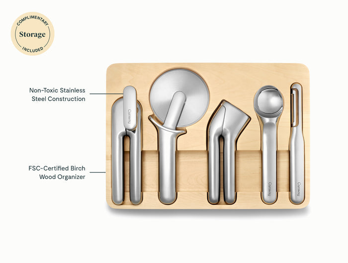The Caraway 5-Piece Stainless Steel Kitchen Gadget Set includes a pizza cutter, peeler, garlic press, ice cream scoop, and can opener in a birch wood FSC-certified organizer; all tools made from non-toxic stainless steel.