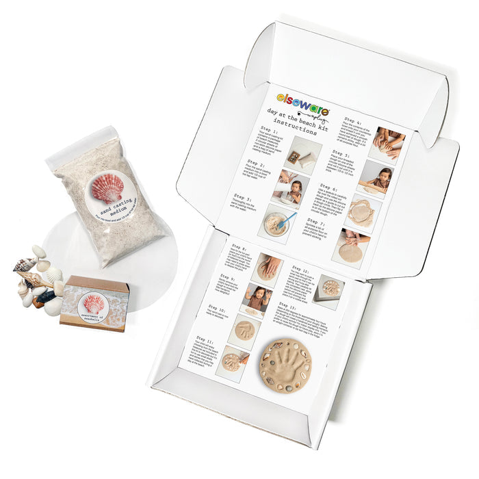 The Elseware Unplug A Day at the Beach Set includes an open kit box with illustrated instructions, a bag of “beach casting sand,” a small box, and assorted beach treasures and seashells displayed on a white background.