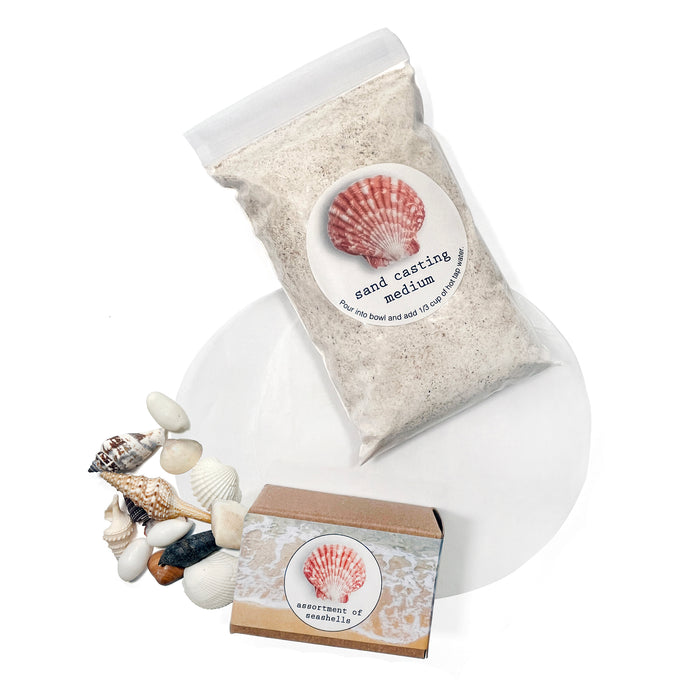 The A Day at the Beach Set by Elseware Unplug includes sand casting medium, a small brown box of assorted seashells, beach treasures, and a white casting mold displayed on a white background.