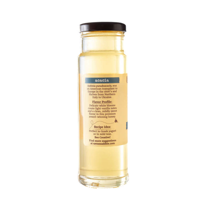 A glass jar of Savannah Bee Companys Acacia Honey with a black lid. The label details its origin, flavor profile, and provides recipe ideas. Pair its mild sweetness with Greek yogurt or tea for an unparalleled taste experience, noting its unique high fructose content.