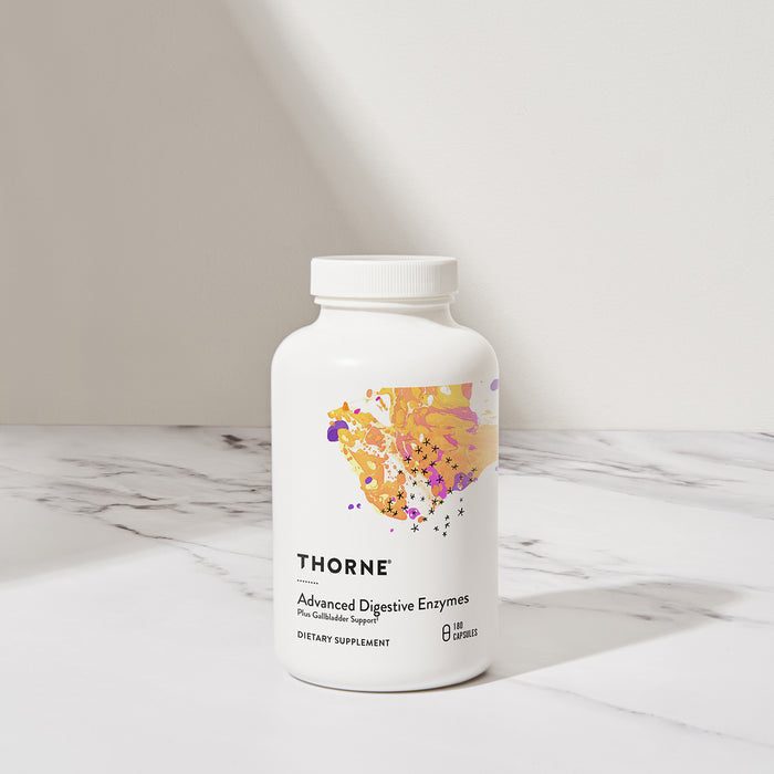 A Thorne Advanced Digestive Enzymes bottle sits on a marble surface, offering digestion support. Its label features a colorful abstract design with yellow and purple accents, stating Dietary Supplement, while the softly lit background adds to its charm.