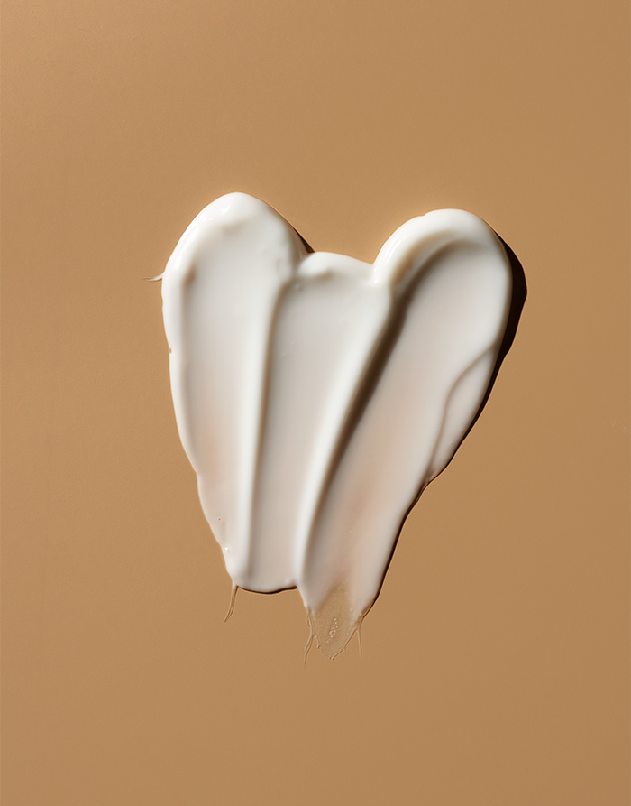 OSEAs Advanced Repair Eye Cream, known for reducing puffiness and its anti-aging properties, is smeared in a heart shape on a smooth, light brown surface. Its glossy texture stands out against the warm background.