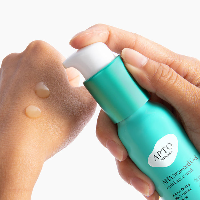 A hand pumps gel from a blue bottle labeled APTO Skincare AHA Seaweed Gel, showcasing skincare benefits as two drops glisten on the skin against a white backdrop. The Resurfacing & Deeply Exfoliating Formula highlights its cruelty-free nature.