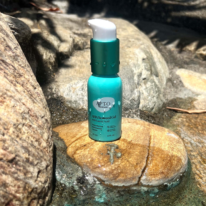APTO Skincares cruelty-free AHA Seaweed Gel with Lactic Acid, a resurfacing and deeply exfoliating formula, sits on a rock. The green bottle with a white pump cap is surrounded by stones in dappled sunlight, reflecting natures tranquility.
