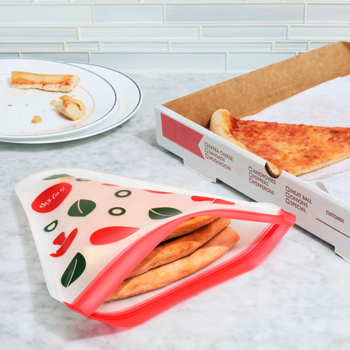 The (re)zip Airtight Pizza Saver Kit holds leftover pizza slices on the countertop, beside a pizza box with one slice and a plate of pizza crusts.