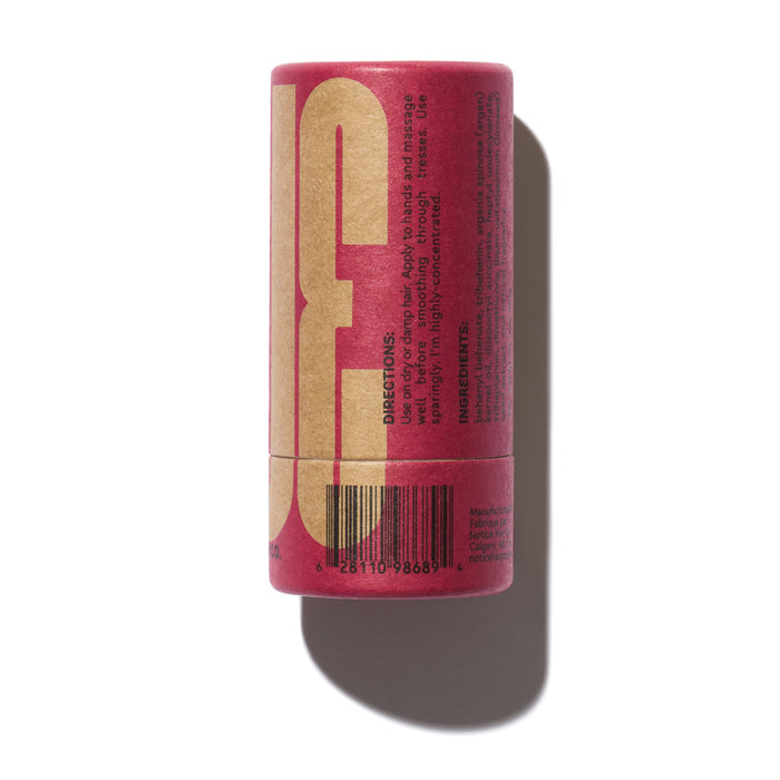 A cylindrical red tube of ALINE Solid Hair Oil by NOT!CE Hair Co stands upright, featuring directions and ingredients on its beige and red label. Its sleek design is highlighted against a clean white background, casting a shadow to the right.