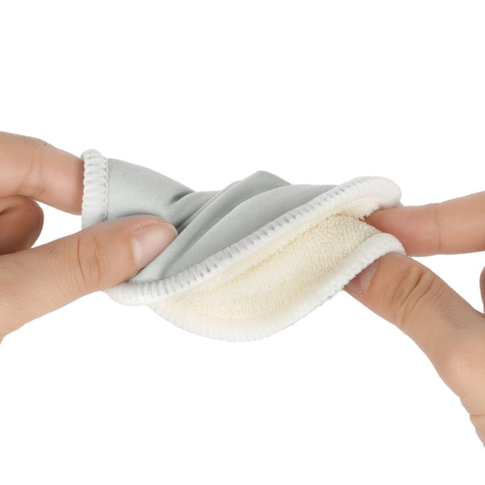 Close-up of hands holding a Haakaa All-Day Reusable Nursing Pad in light blue and white, bent slightly to display its soft microfiber texture and stitching detail.