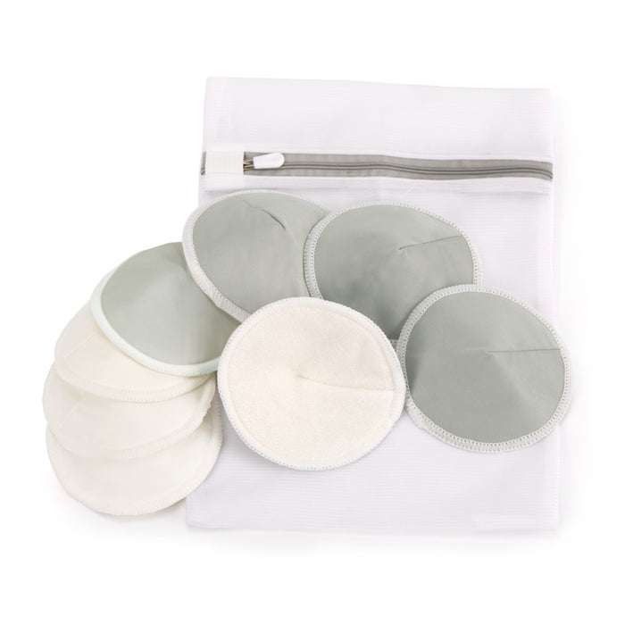 Haakaas All-Day Reusable Nursing Pads, made from absorbent microfiber and bamboo, are displayed on a white surface. Some are stacked, others spread out to highlight their eco-friendly design, with a white mesh laundry bag complete with a zipper positioned behind them for added convenience.