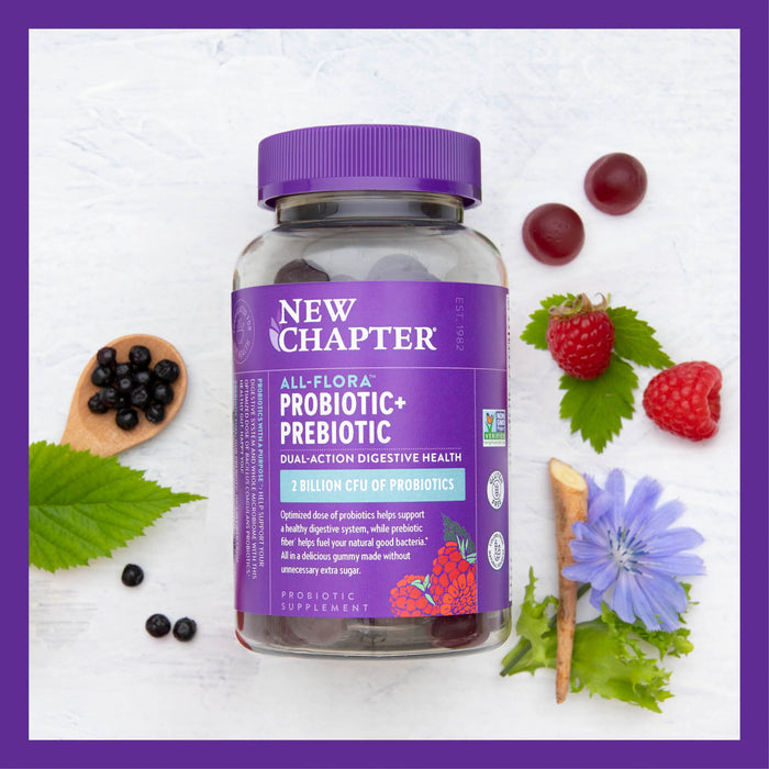 New Chapters All Flora Probiotic + Prebiotic stands among raspberries, blueberries, and vibrant flowers on a light surface. Its label highlights 2 billion CFU for digestive health and prebiotic inulin fiber to enhance your gut.