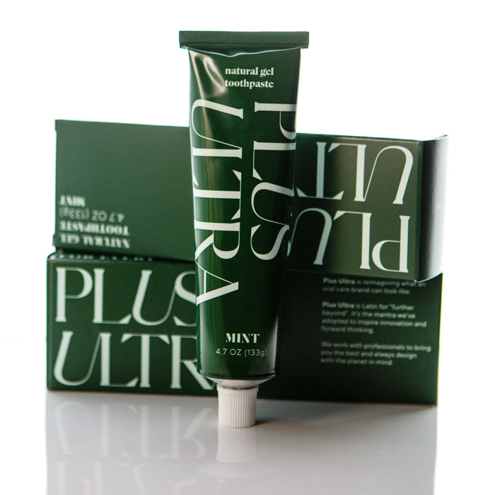 The green tube of All Natural Gel Toothpaste from Plus Ultra, labeled Mint, stands upright with white text beside its matching box, promising to whiten your smile with a minty fresh formula as it glistens on a glossy surface.