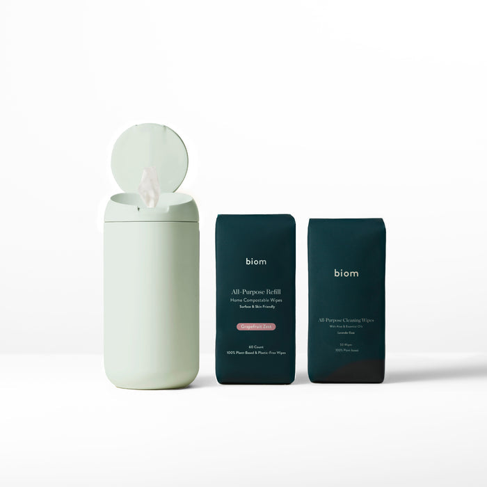An open mint green container reveals a wipe next to two dark green packets labeled Biom, identified as All-Purpose Wipe Refills made from natural ingredients, all on a plain white background.
