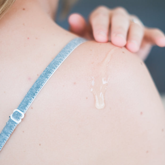 A person in a blue spaghetti strap top gently applies Beauty by Earths Aloe Vera Gel to their shoulder. The freckled skin glistens, highlighted by the clear, organic skincare product, while fingernails shimmer with traces of the gel.