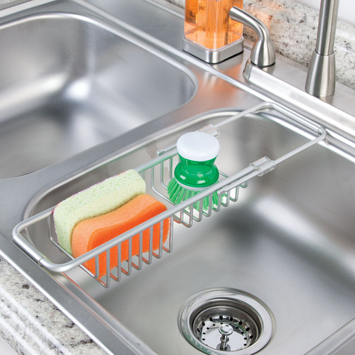 The rust-resistant Aluminum Over The Sink Basket by iDesign features a drain basket storage rack that holds three sponges and a soap dispenser with a green lid, complementing the gray speckled countertop and the faucet on the right.