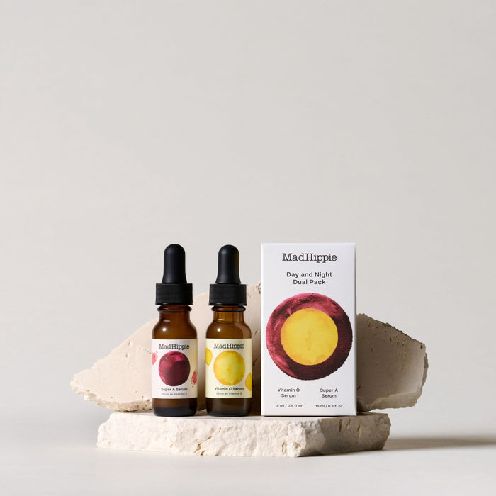 Two Mad Hippie AM PM Dual Pack serum bottles sit on textured stone slabs against a neutral backdrop. The box reads AM PM Dual Pack, containing Vitamin C Serum with antioxidants and Vitamin A Serum, creating a minimalist and elegant display.