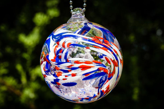 Hanging American Confetti Orb with red white and blue swirls and ashes inside, outdoors.