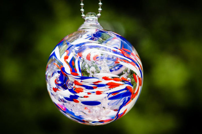 Close-up of American Confetti Orb with red white and blue swirls against a blurred green background.
