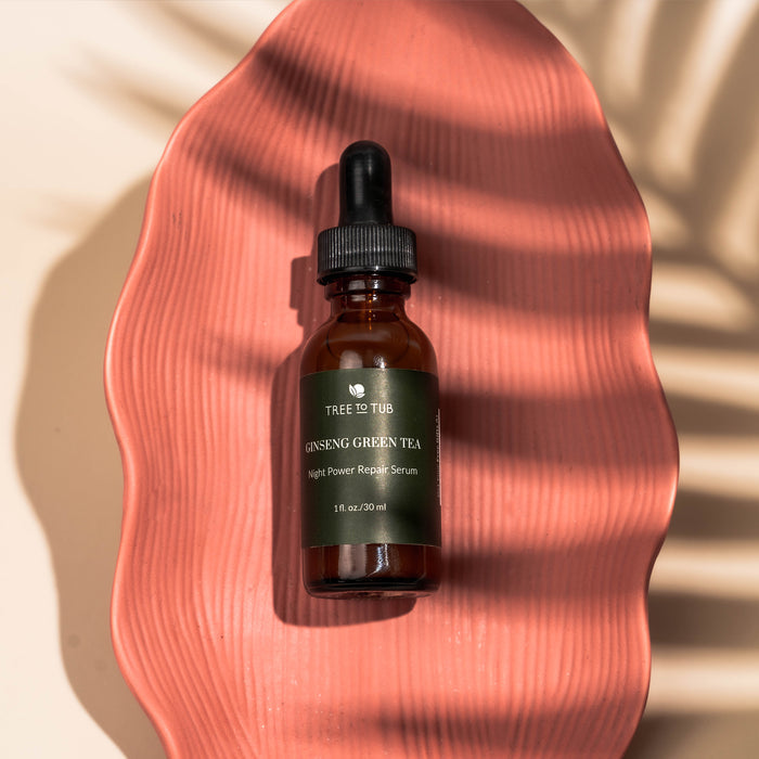 A dropper bottle labeled Tree To Tub Anti Aging Green Tea, Hyaluronic & Retinol Serum for Face sits on a textured pink surface with palm leaf shadows, creating a tropical vibe. Ideal for sensitive skin, this anti-aging serum rejuvenates your complexion overnight.