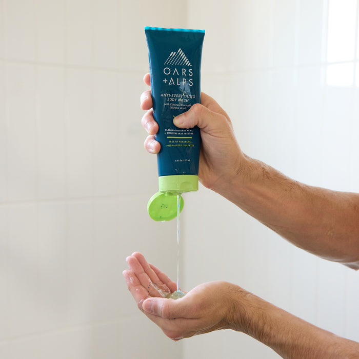 Someone squeezes Oars + Alps Anti-Everything Body Wash into their hand while showering against white tiled walls.