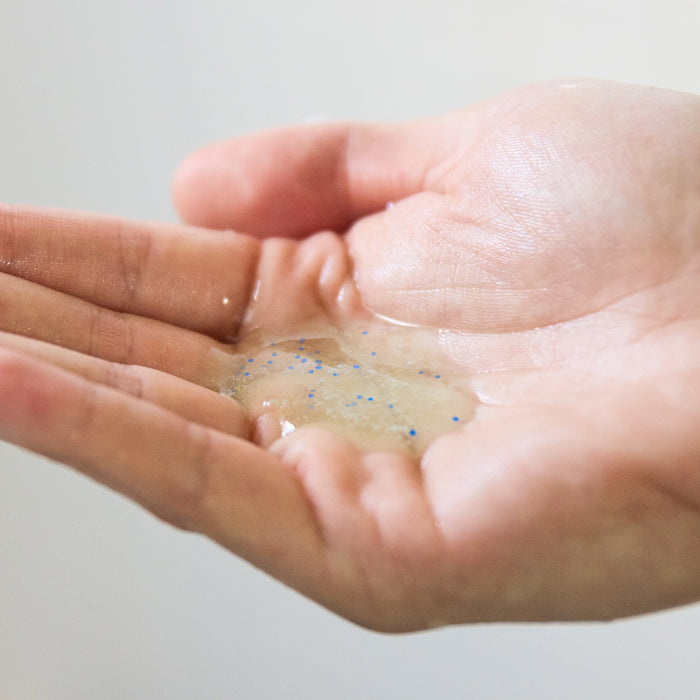 A close-up of an open hand holding a small amount of Oars + Alps Anti-Everything Body Wash, a clear gel with blue microbeads, likely featuring Salicylic Acid to exfoliate and help clear skin.