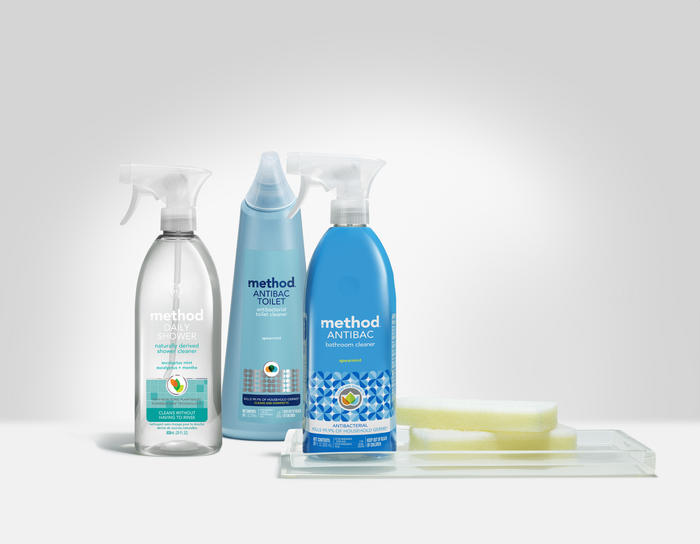 Displayed are three method cleaning products: a daily shower spray, an antibacterial toilet cleaner, and a paraben-free Antibacterial Bathroom Cleaner. A sponge sits on a clear tray beside them against a light gray background.