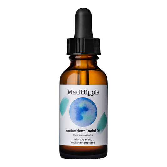 A brown glass dropper bottle labeled Mad Hippie Antioxidant Facial Oil features a blue circle with teal geometric shapes and contains natural ingredients such as argan oil, goji, and hemp seed, offering skin hydration with every drop.