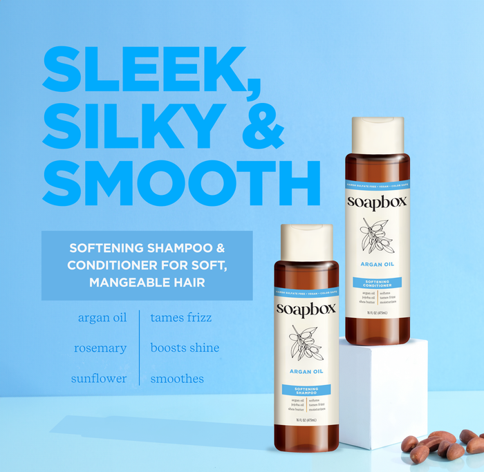 Two bottles featuring Soapbox Argan Oil Softening Conditioner against a blue background highlight benefits: taming frizz, boosting shine, smoothing hair with a vitamin complex. Key ingredients: argan oil, rosemary, and sunflower.