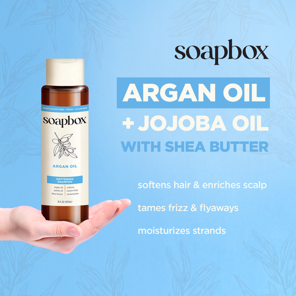A bottle of Soapbox Argan Oil Softening Shampoo with vitamin complex is featured against a blue background, highlighting its benefits: softens hair, enriches scalp, tames frizz and flyaways, and moisturizes strands.