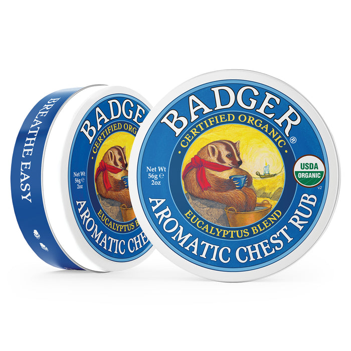 Two tins of Badger Balms Aromatic Chest Rub, featuring a eucalyptus blend, are displayed with an illustrated badger holding a cup. The organic-certified packaging highlights the herbal balms soothing power, with one tin slightly opened to showcase its essential oils.