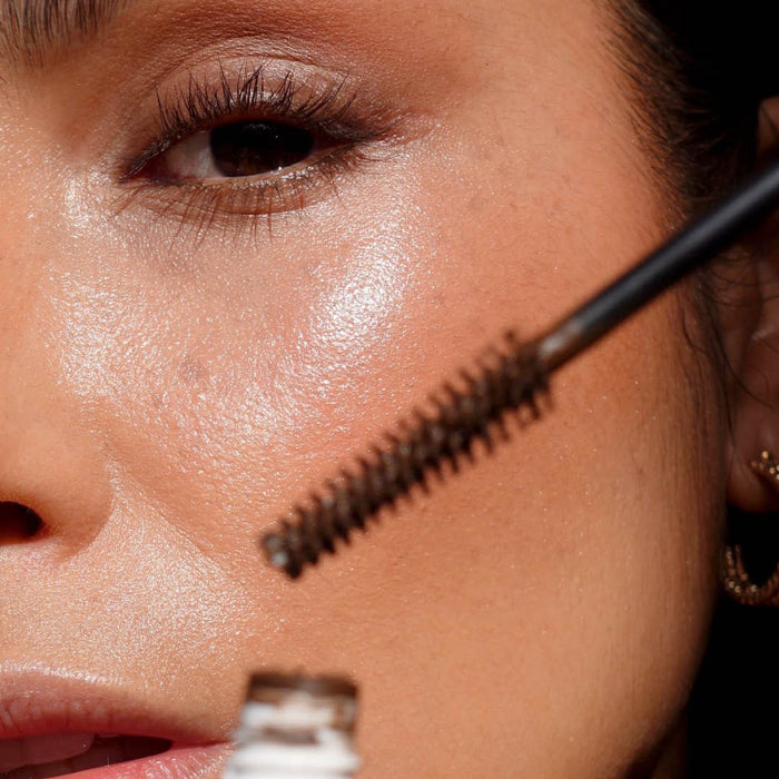Close-up of a person applying Ere Perezs Avocado Waterproof Mascara to their eyelashes. The focus is on one eye with natural makeup and smooth skin, as the applicator brush with a vegan formula nears the lashes, highlighting the skins texture and sheen in good lighting.